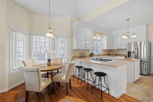 kitchen with white appliances, a peninsula, light countertops, white cabinetry, and backsplash