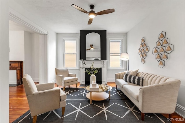 living area with a fireplace, wood finished floors, a ceiling fan, and baseboards