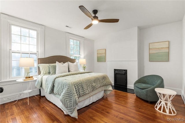 bedroom with wood-type flooring, a fireplace, visible vents, and ceiling fan