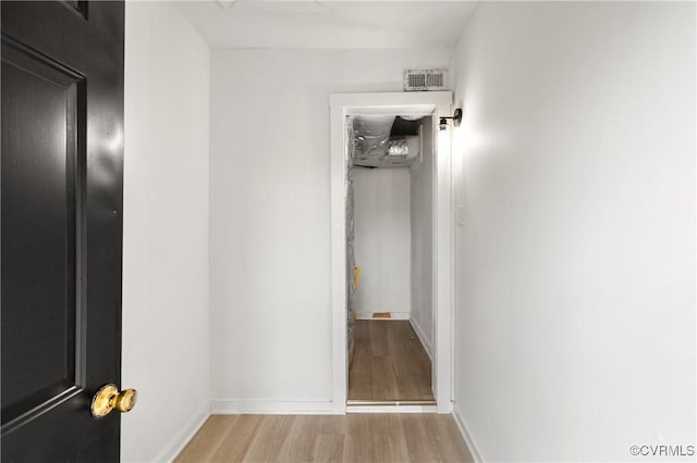 hall featuring light wood-style floors, baseboards, and visible vents