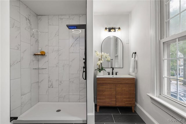 bathroom featuring tile patterned flooring, a tile shower, vanity, and baseboards