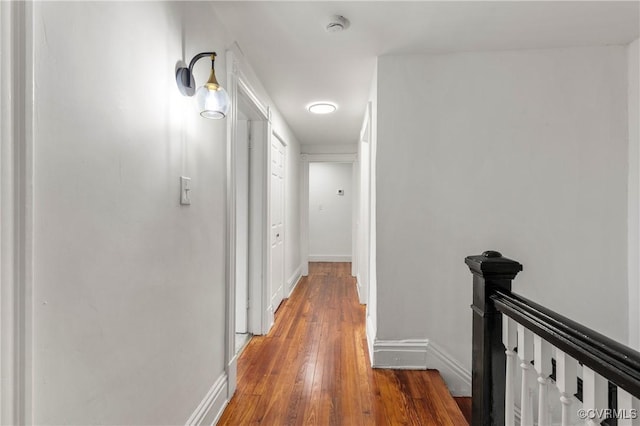 hallway featuring light wood-style flooring, baseboards, and an upstairs landing