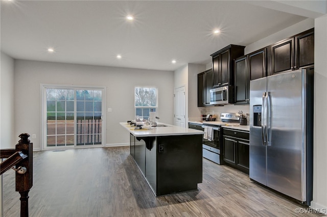 kitchen featuring recessed lighting, stainless steel appliances, light wood-style floors, light countertops, and an island with sink