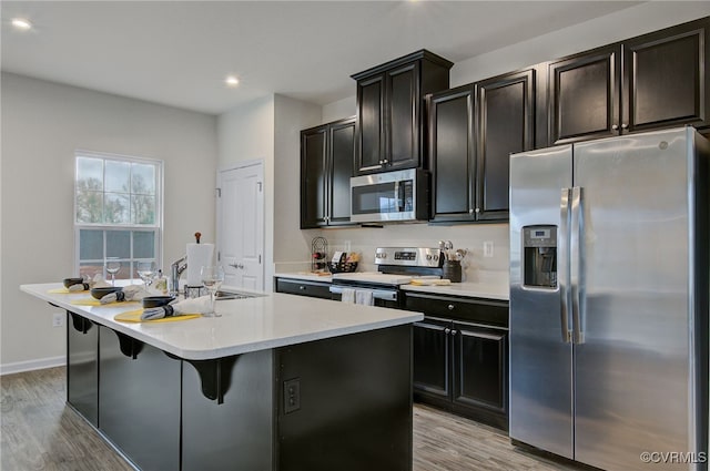 kitchen featuring light wood finished floors, light countertops, appliances with stainless steel finishes, an island with sink, and a kitchen bar