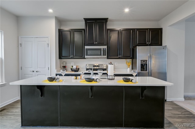 kitchen with dark wood-style floors, stainless steel appliances, light countertops, and a center island with sink