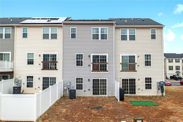 rear view of property with central AC, fence, and solar panels