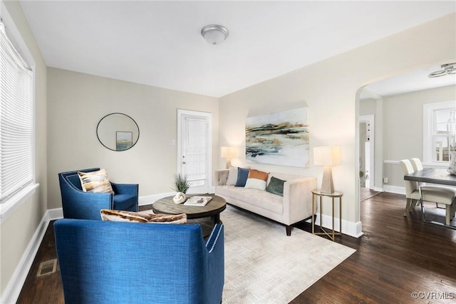 living room featuring arched walkways, wood finished floors, visible vents, and baseboards