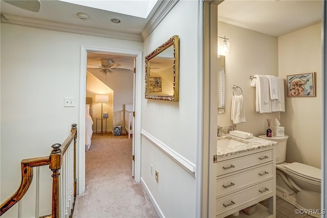 hallway featuring a sink, a skylight, crown molding, baseboards, and light colored carpet