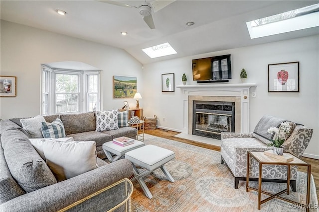 living room with lofted ceiling with skylight, wood finished floors, a high end fireplace, recessed lighting, and baseboards