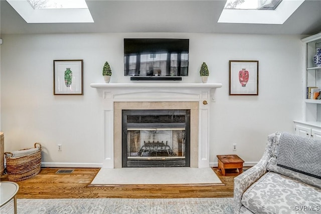 living room featuring visible vents, wood finished floors, a skylight, and a fireplace