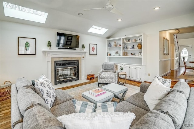 living area with a high end fireplace, ceiling fan, recessed lighting, vaulted ceiling with skylight, and light wood-style flooring