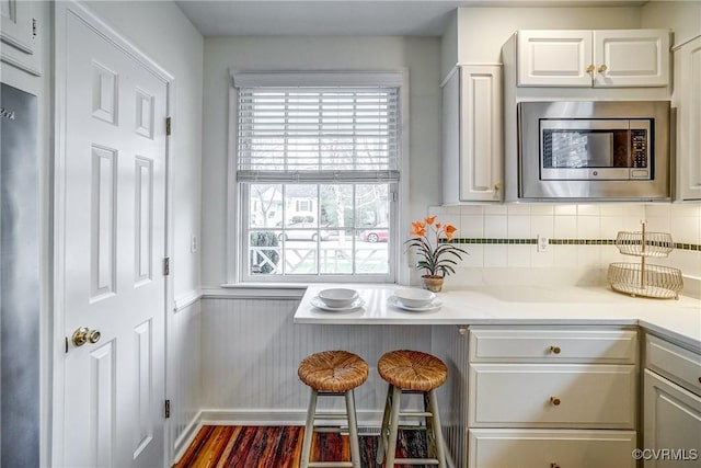 kitchen featuring tasteful backsplash, stainless steel microwave, wainscoting, white cabinets, and dark wood-style flooring