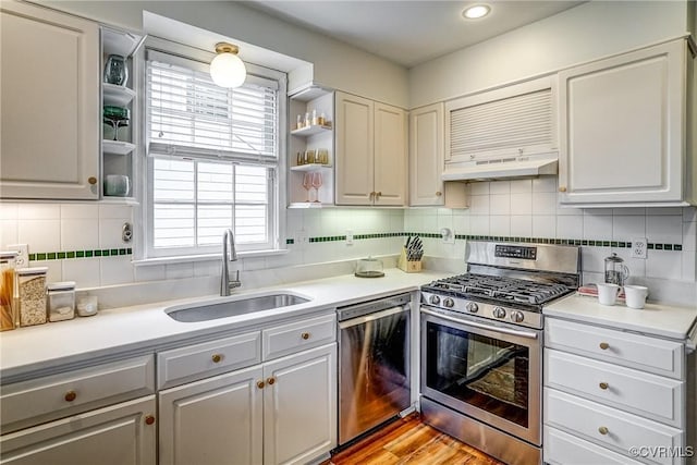 kitchen featuring open shelves, a sink, stainless steel appliances, under cabinet range hood, and tasteful backsplash