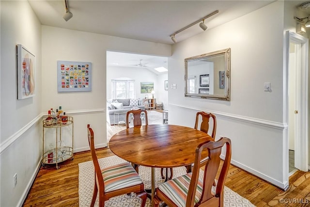 dining area featuring rail lighting, wood finished floors, a ceiling fan, and vaulted ceiling