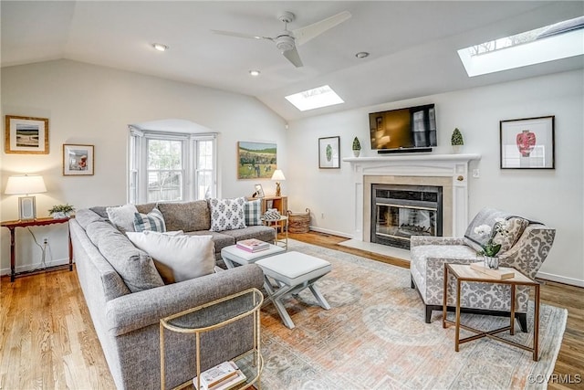 living room with baseboards, lofted ceiling with skylight, a fireplace with flush hearth, wood finished floors, and a ceiling fan