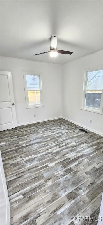 empty room featuring ceiling fan, baseboards, wood finished floors, and a healthy amount of sunlight