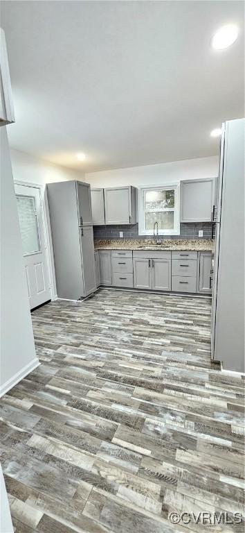 kitchen with gray cabinets, a sink, backsplash, and wood finished floors