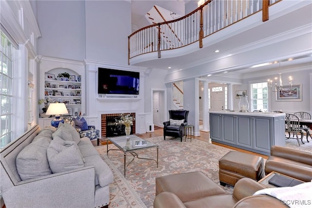 living room with built in shelves, ornamental molding, stairway, a brick fireplace, and an inviting chandelier