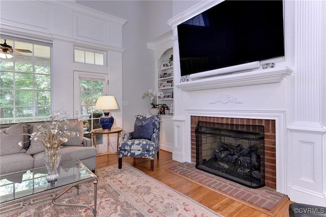 living area with a ceiling fan, a towering ceiling, wood finished floors, built in shelves, and a fireplace