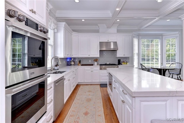 kitchen featuring under cabinet range hood, stainless steel appliances, a sink, a center island, and beamed ceiling