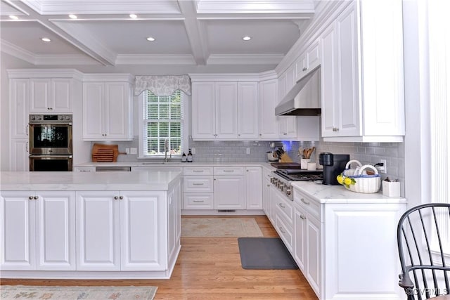 kitchen featuring stainless steel double oven, under cabinet range hood, gas stovetop, white cabinetry, and beam ceiling