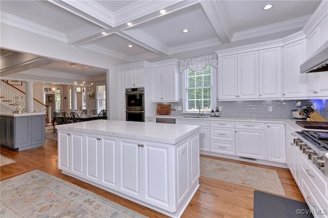 kitchen featuring a sink, a kitchen island, appliances with stainless steel finishes, light wood finished floors, and beamed ceiling