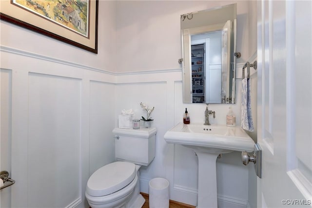 half bath featuring a wainscoted wall, a decorative wall, and toilet