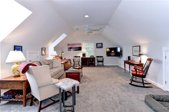 carpeted living room with ceiling fan, vaulted ceiling with skylight, and baseboards