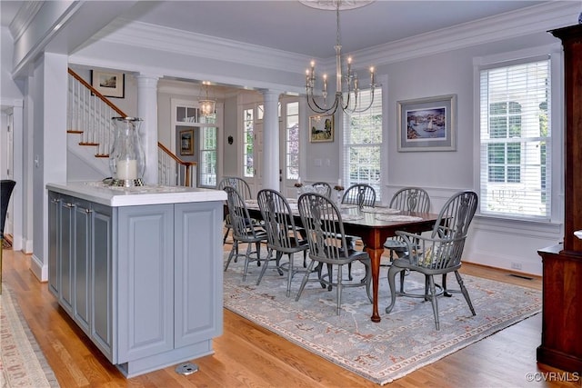 dining room featuring stairs, light wood-type flooring, ornate columns, an inviting chandelier, and crown molding