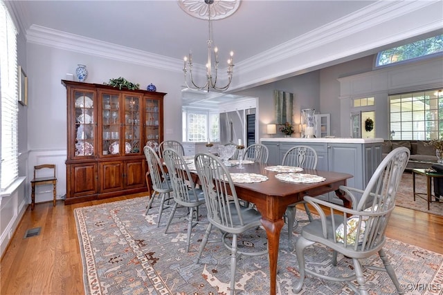 dining space with a wainscoted wall, crown molding, visible vents, light wood finished floors, and an inviting chandelier