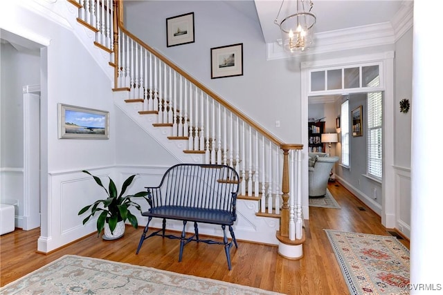 foyer featuring crown molding, a towering ceiling, wood finished floors, a chandelier, and stairs