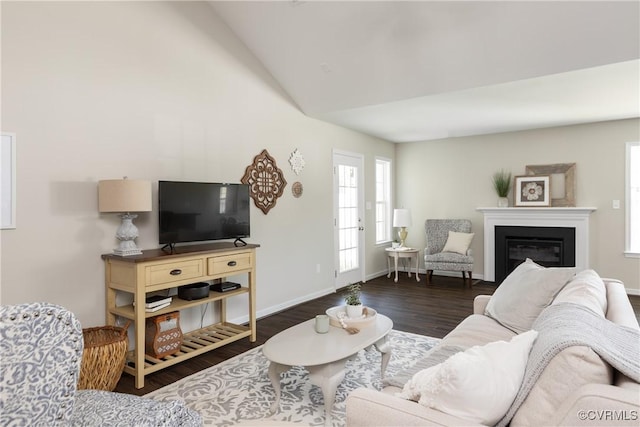 living area featuring lofted ceiling, a glass covered fireplace, wood finished floors, and baseboards