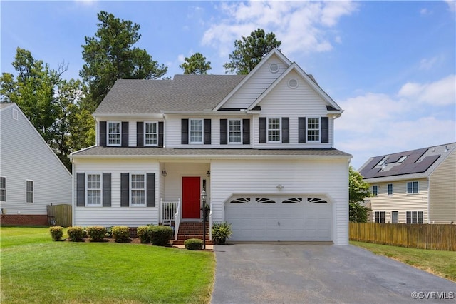 traditional-style house featuring roof with shingles, an attached garage, fence, driveway, and a front lawn