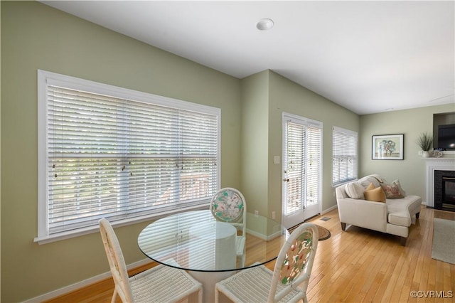 dining room featuring light wood-type flooring, a glass covered fireplace, and baseboards