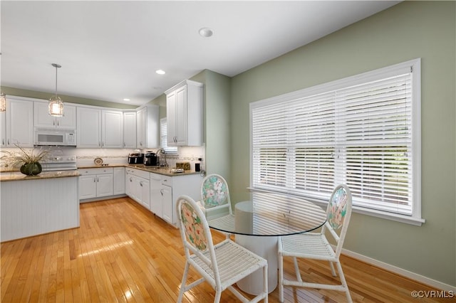 kitchen featuring white appliances, light wood finished floors, baseboards, white cabinets, and backsplash