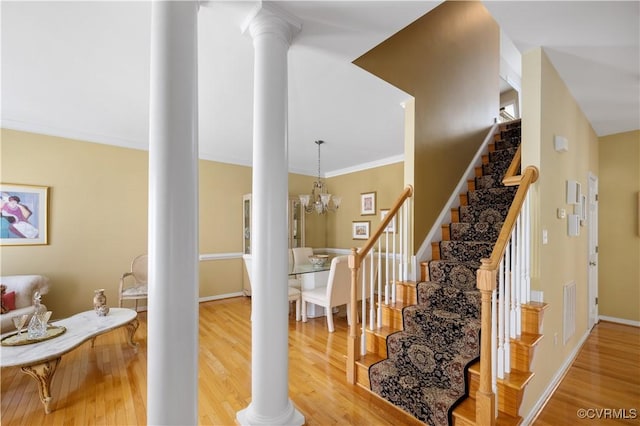 stairs with a notable chandelier, baseboards, wood finished floors, and ornate columns