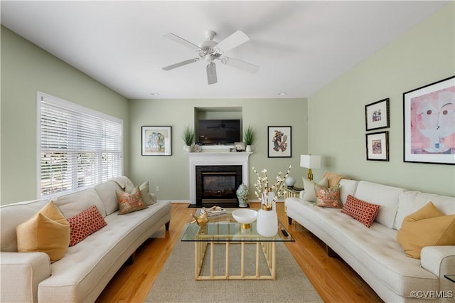 living area featuring a fireplace with flush hearth, ceiling fan, wood finished floors, and baseboards