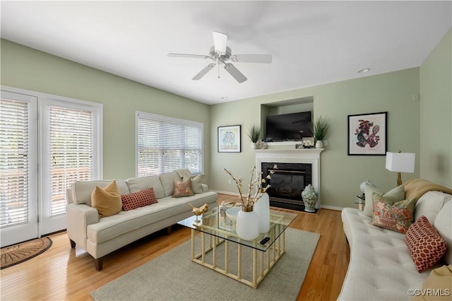 living room featuring ceiling fan, baseboards, wood finished floors, and a glass covered fireplace