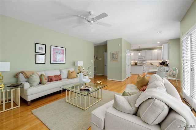 living area featuring visible vents, light wood finished floors, a ceiling fan, and baseboards