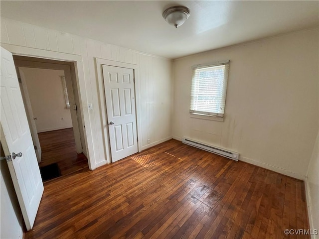 unfurnished bedroom with dark wood-style flooring, baseboard heating, a closet, and baseboards