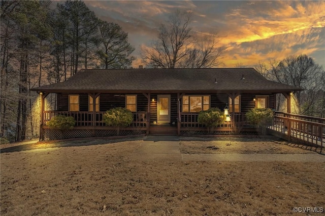 rustic home with covered porch, a shingled roof, and log veneer siding