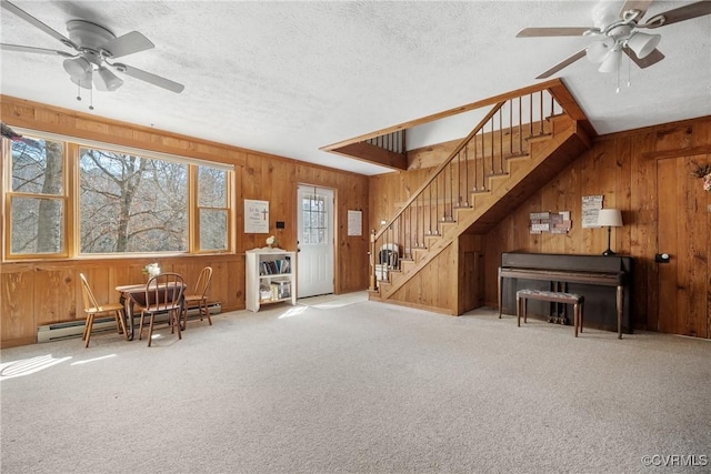 unfurnished living room featuring a textured ceiling, a baseboard heating unit, wood walls, carpet flooring, and stairway