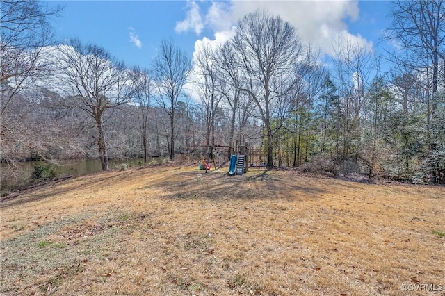 view of yard featuring playground community and a wooded view