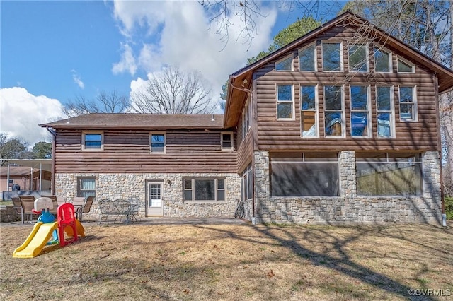 rear view of house with stone siding and a yard