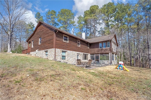 rear view of house with a patio area, stone siding, a lawn, and a chimney