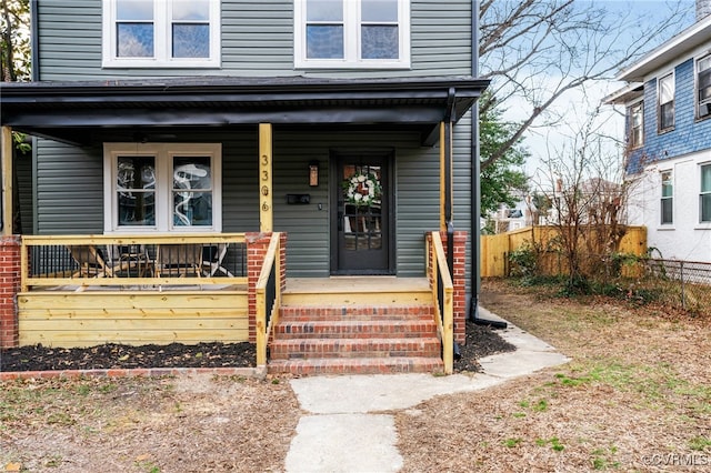 view of exterior entry featuring covered porch and fence