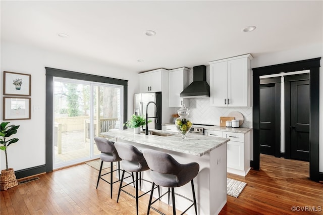 kitchen with visible vents, light wood-type flooring, stainless steel refrigerator with ice dispenser, backsplash, and wall chimney exhaust hood