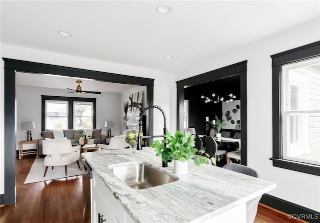 kitchen with dark wood-style flooring, stainless steel dishwasher, white cabinets, a sink, and light stone countertops