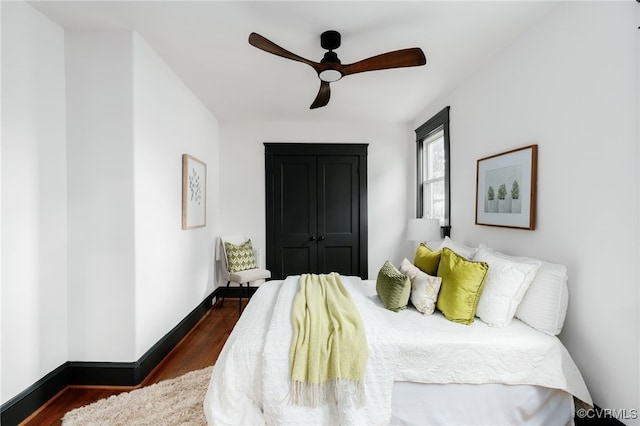 bedroom with dark wood-type flooring, a ceiling fan, and baseboards