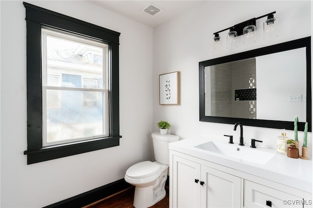 bathroom with toilet, vanity, visible vents, and baseboards